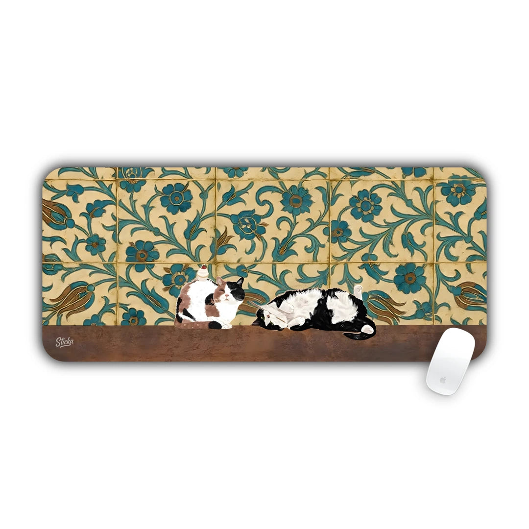 Two calico cats lying in front of a floral green and gold tile wall desk pad 70x30